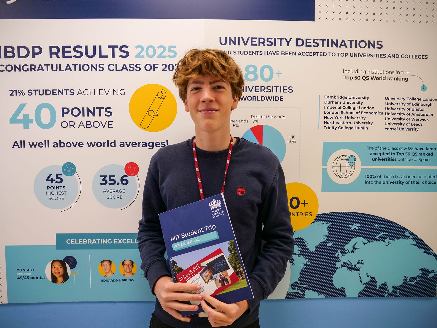 A student smiling in front of the camera holding information papers from MIT