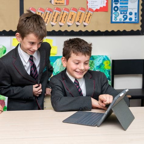 two male students in blazer and school uniform, using tablet to collaborate during lesson