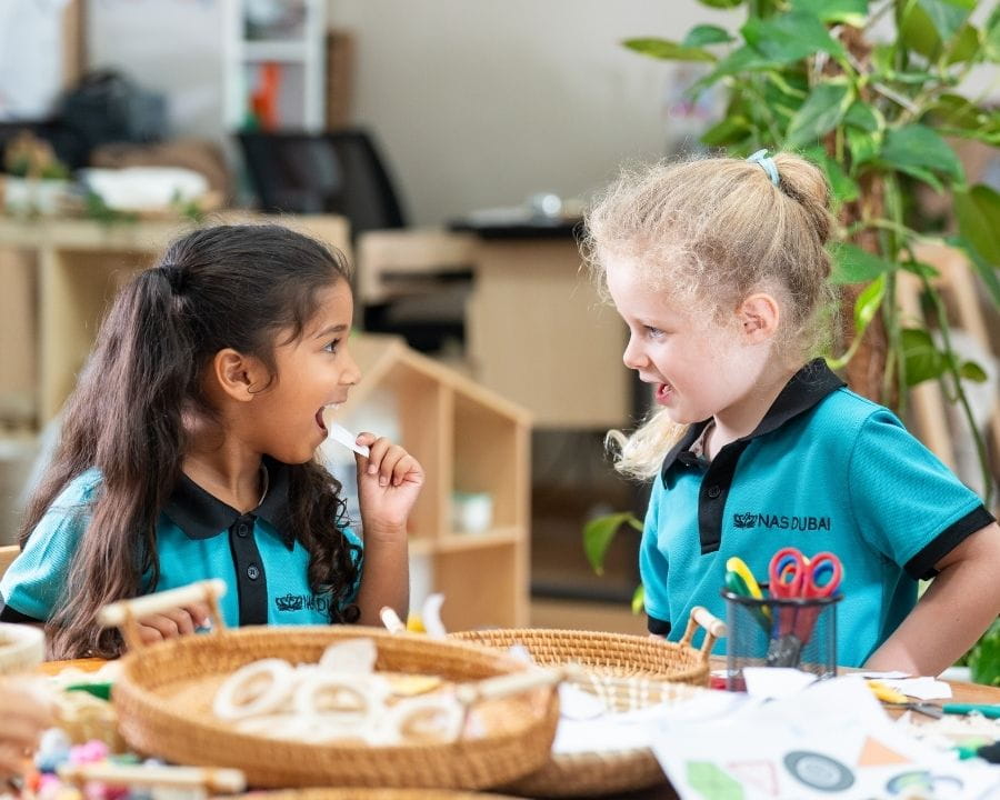 Young students in NAS Dubai school uniforms enjoying a hands‑on learning activity in an early years classroom at a British international school in Dubai.