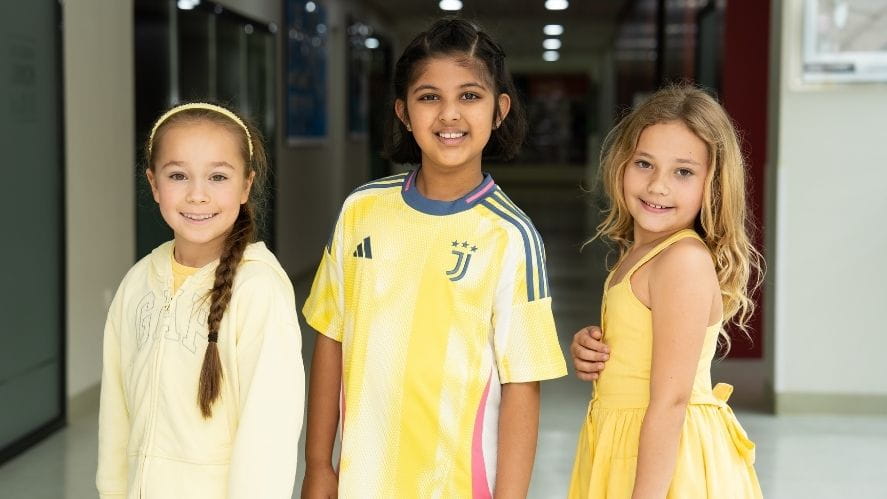 Three students standing in a school hallway wearing yellow outfits to support Childhood Cancer Awareness Day.