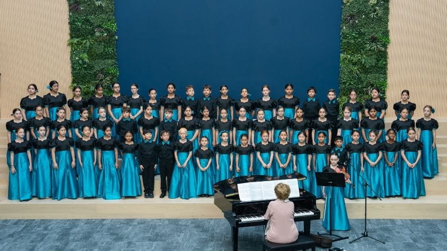 NAS Dubai Giocoso choir dressed in matching teal and black concert attire present a coordinated musical piece on stage. 