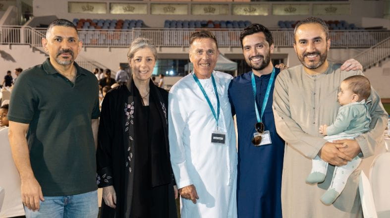 Group photo of NAS Dubai staff and community members standing together at the school’s community iftar, with the principal included, in a large outdoor venue with tables and guests in the background.