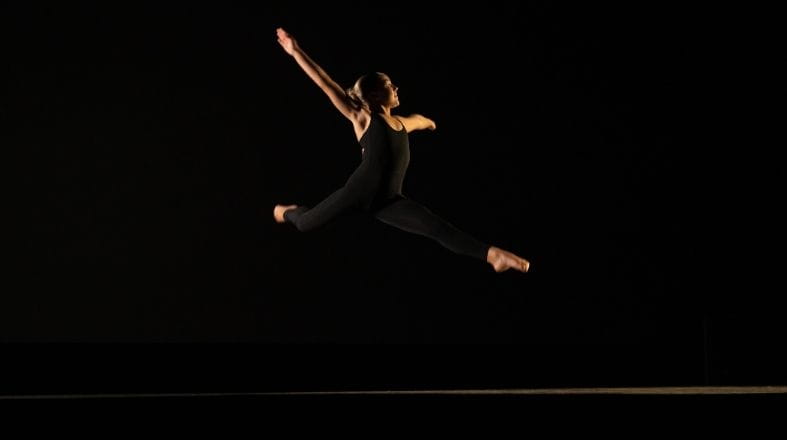 Student performing a dynamic dance leap during training, demonstrating strength, flexibility, and control.