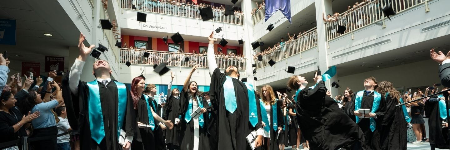 Year 13 students dressed in gowns throwing graduation caps in atrium.