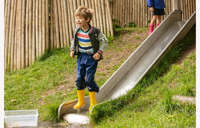 young child on outdoor slide with boots