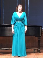 woman singing on stage in a blue dress in front of a piano